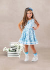 Young girl in a blue floral twirl dress standing next to wooden crates with flowers on a beige background