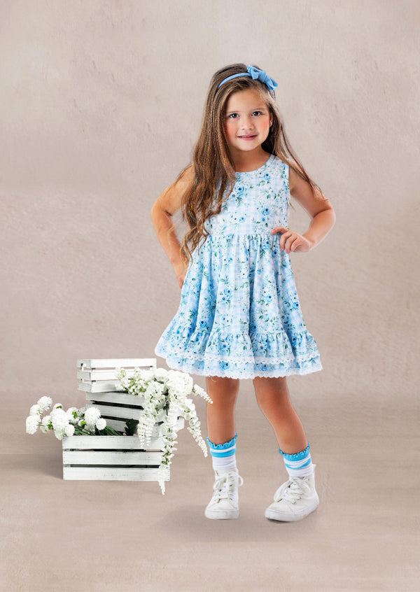 Young girl in a blue floral twirl dress standing next to wooden crates with flowers on a beige background