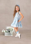 toddler girl in a floral twirl dress standing next to a wooden crate with flowers on a beige background
