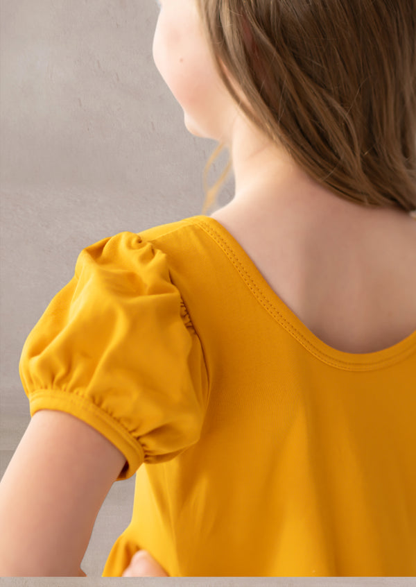 Yellow top with puff sleeves worn by a child against a neutral background