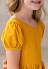 Child wearing a mustard yellow dress with puff sleeves against a neutral background