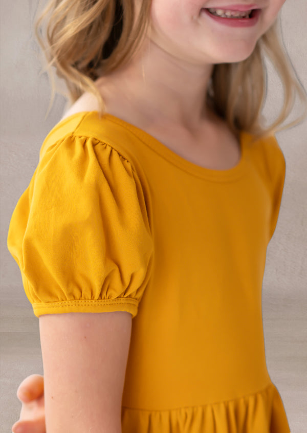 Child wearing a mustard yellow dress with puff sleeves against a neutral background