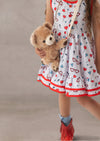 Child wearing a dress with heart patterns print is holding a teddy bear purse against a neutral background