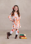 Toddler girl in a floral twirl dress standing next to stacked books on a beige background