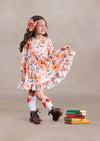 Young girl in a floral dress standing next to stacked books on a beige background