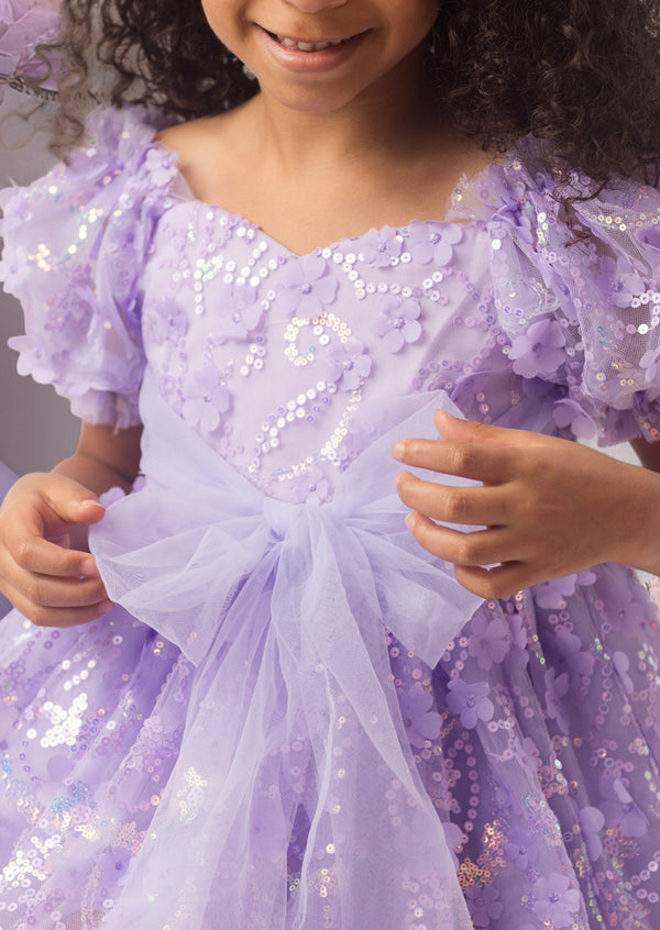 Child wearing a sparkling purple party dress with a bow detail.