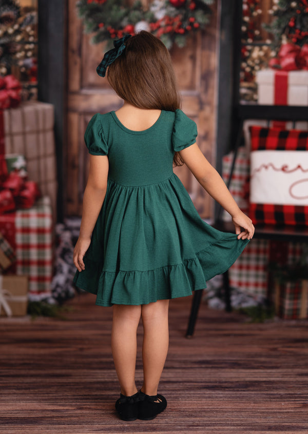 Child wearing a green dress in a festive setting with Christmas decorations.