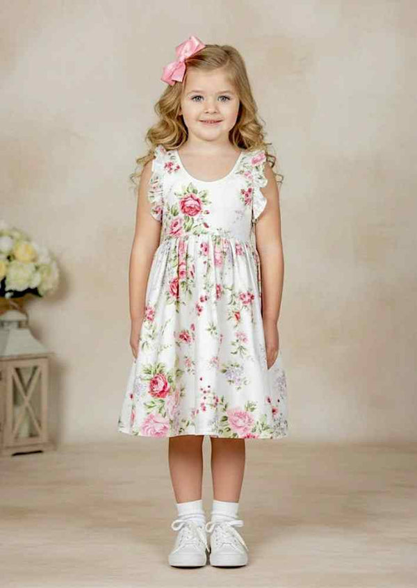 Child wearing a white cotton dress with pink rose print and ruffle shoulder ties outdoors