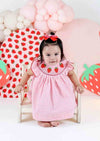 Baby girl wearing pink strawberry smocked dress with embroidered strawberries and pink check pattern