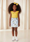 Woman wearing yellow off-shoulder top with buttons and light blue floral bow skirt outdoors