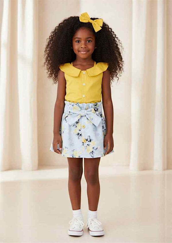 Woman wearing yellow off-shoulder top with buttons and light blue floral bow skirt outdoors