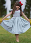 Little girl wearing gray Alice Hand Smocked Dress with red embroidery and matching bow in outdoor setting