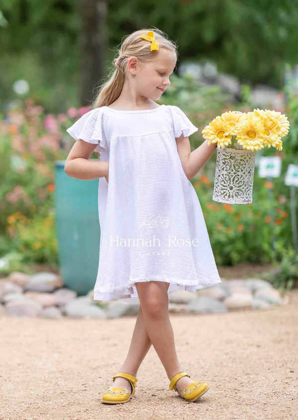 Young girl wearing white organic cotton dress holding yellow flowers outdoors